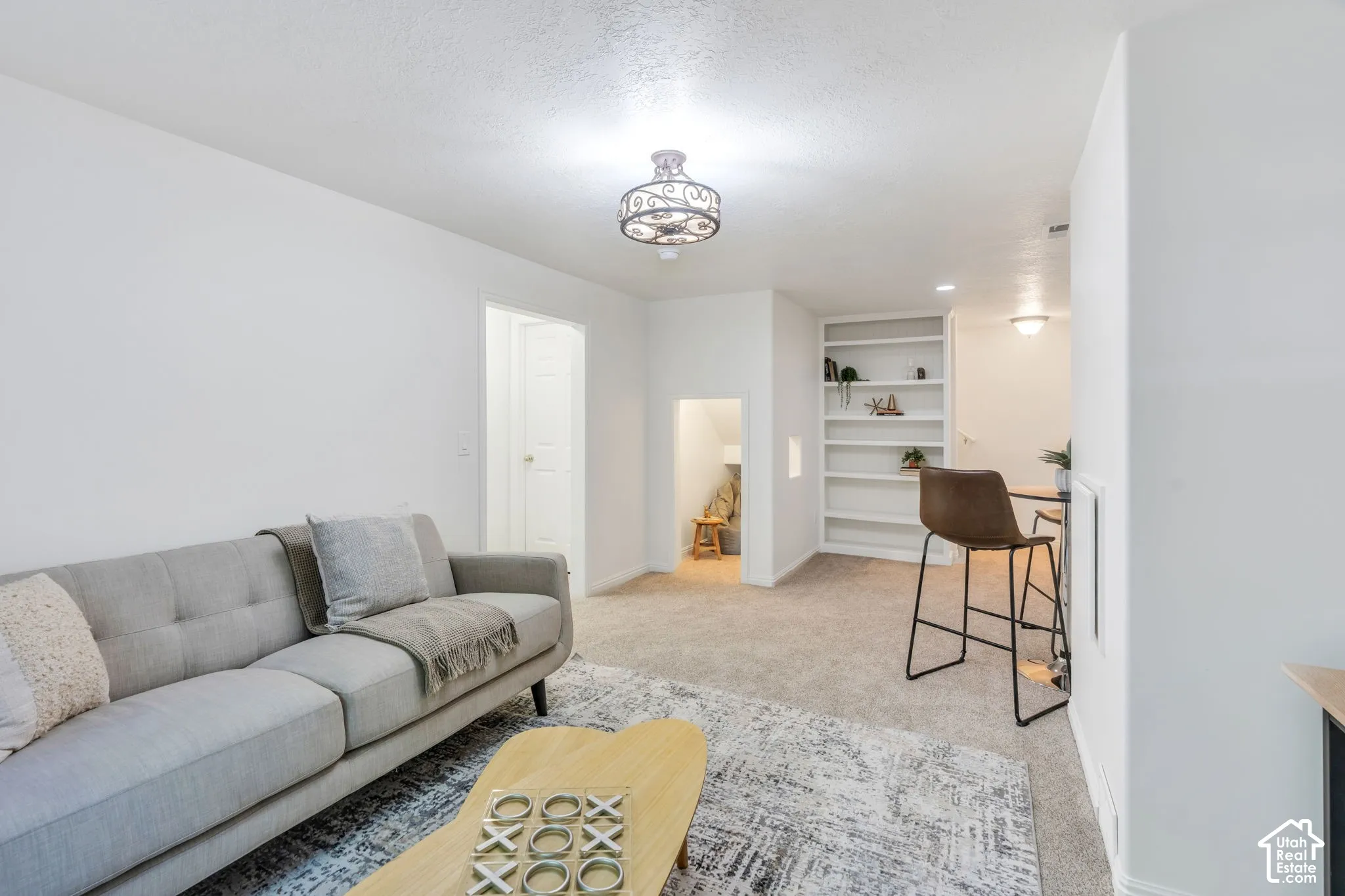 Spacious living area featuring neutral carpeting, white walls, and an ornate ceiling fixture