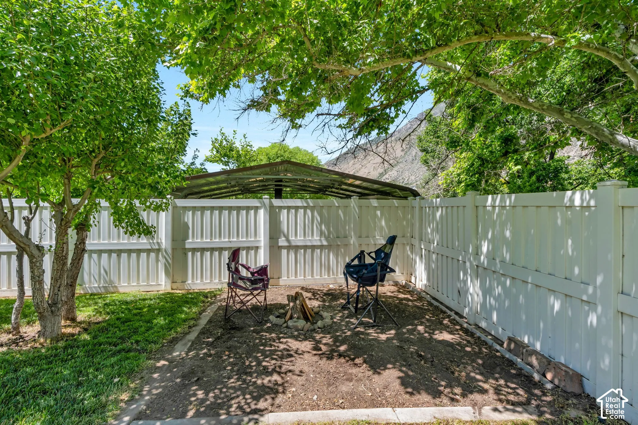 Private outdoor area featuring a white privacy fence, mature trees, and a shaded open space