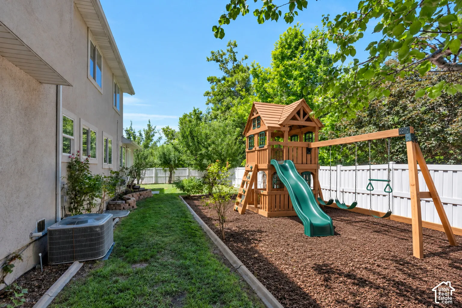 Side yard featuring a white vinyl privacy fence, mulched play area, and a lawn border