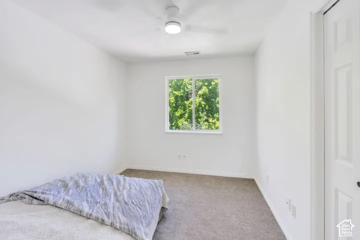 Bright room featuring a window overlooking greenery, neutral carpet flooring, white walls, and a ceiling fan with integrated lighting