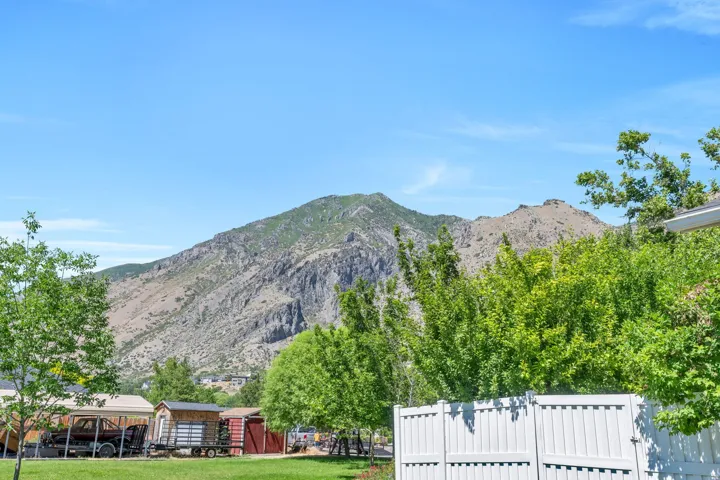 Mountain backdrop with a clear sky, featuring a white vinyl fence and mature green trees