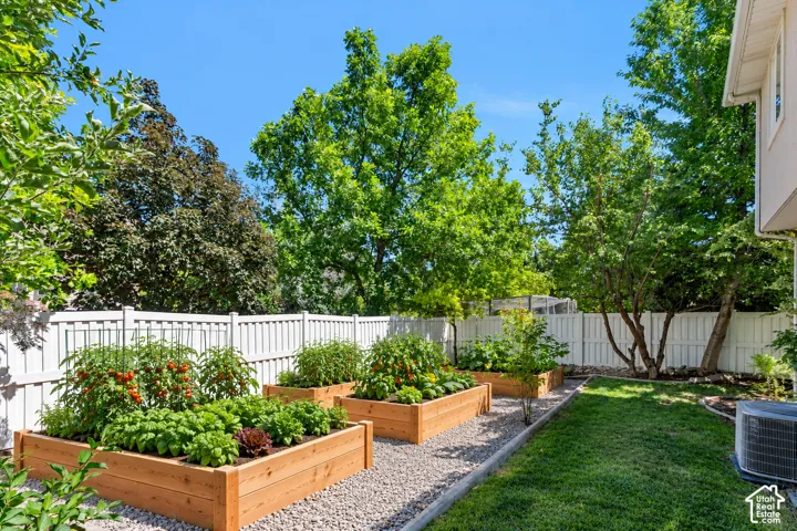 Backyard garden featuring three raised timber planting beds, a gravel garden path, a grass lawn, and white vinyl privacy fencing