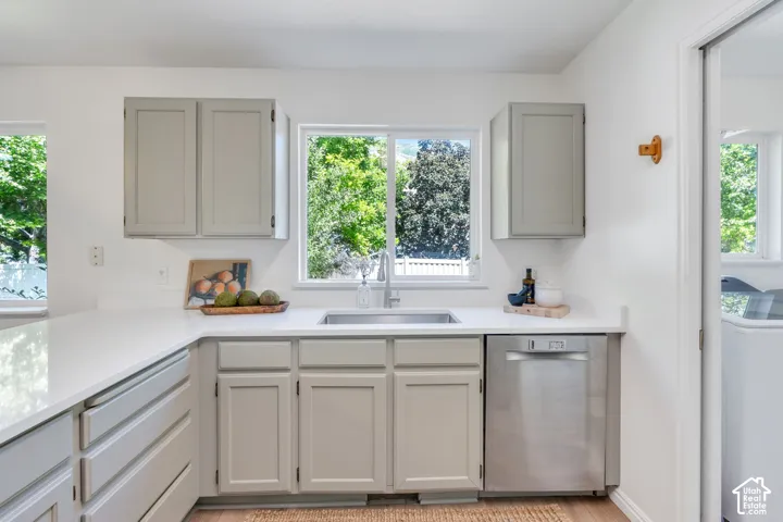 Kitchen featuring light gray cabinetry, white countertops, a stainless steel sink, and a stainless steel dishwasher