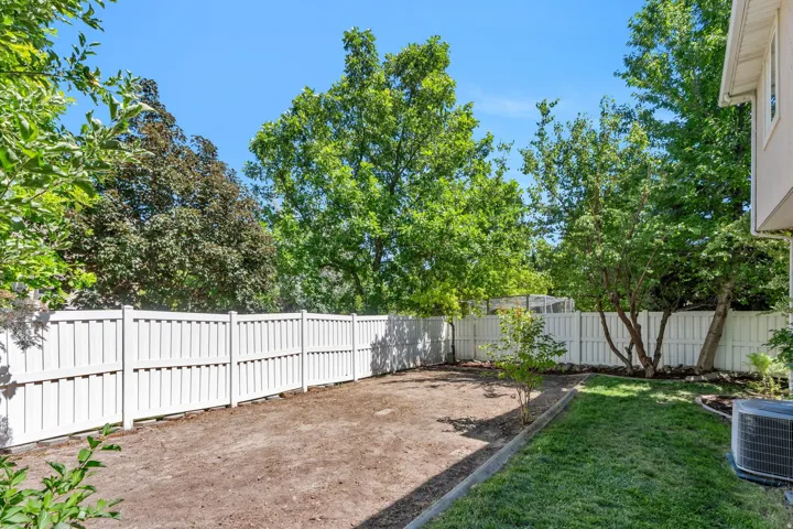 Fenced backyard featuring a partial lawn area, an unlandscaped section, and mature trees providing natural shading