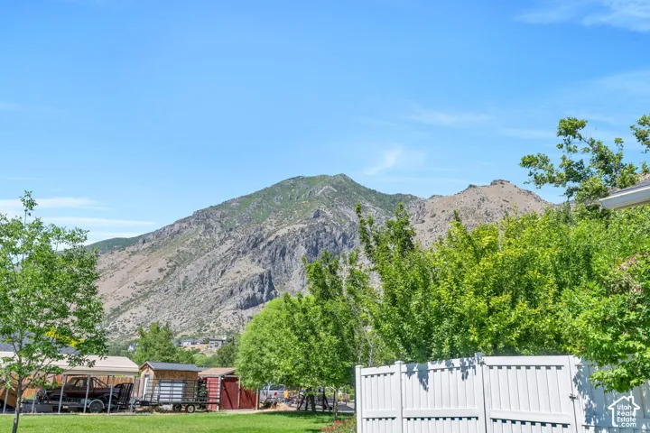 Mountain backdrop with a clear sky, featuring a white vinyl fence and mature green trees