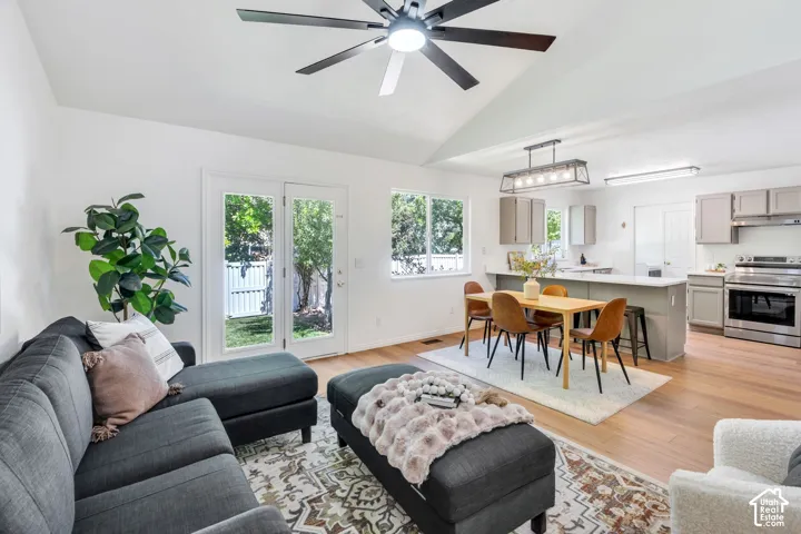 Spacious open-concept living area featuring a vaulted ceiling with a modern ceiling fan, wood-finish flooring, and white walls