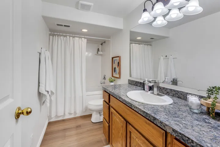 Bathroom featuring a wood-finish vanity with a granite-style countertop, undermount sink, and a framed mirror