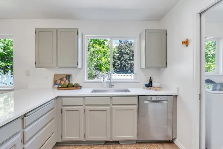 Kitchen featuring light gray cabinetry, white countertops, a stainless steel sink, and a stainless steel dishwasher