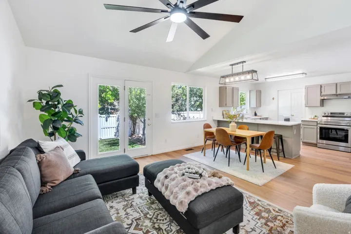 Spacious open-concept living area featuring a vaulted ceiling with a modern ceiling fan, wood-finish flooring, and white walls