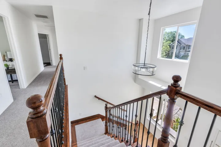 Stairwell featuring wood-finish handrails with iron balusters, a decorative chandelier, and a large window