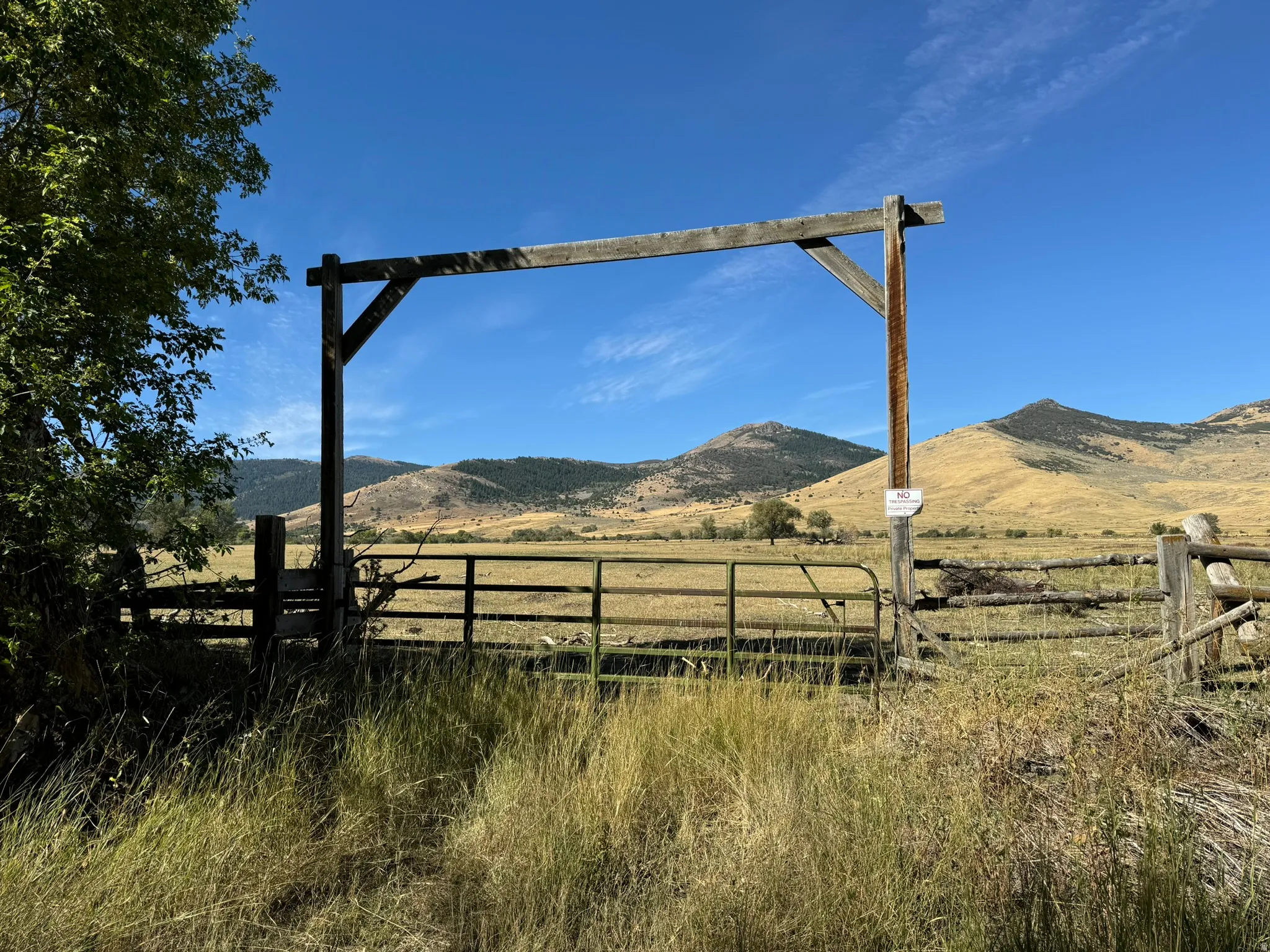 Rustic wood entrance gate with a metal swing gate, set against a backdrop of rolling hills and open fields