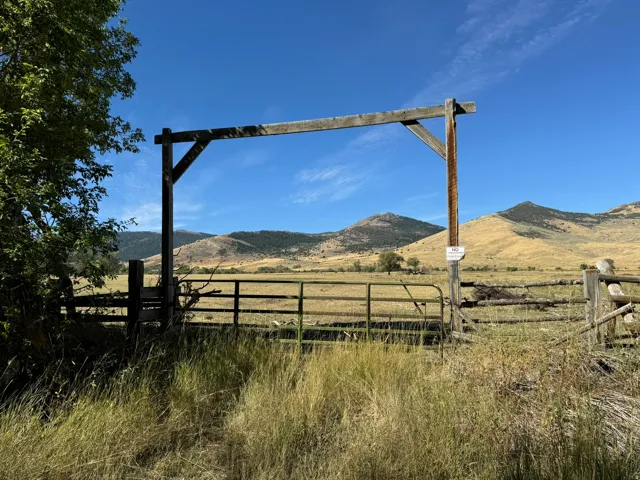 Rustic wood entrance gate with a metal swing gate, set against a backdrop of rolling hills and open fields