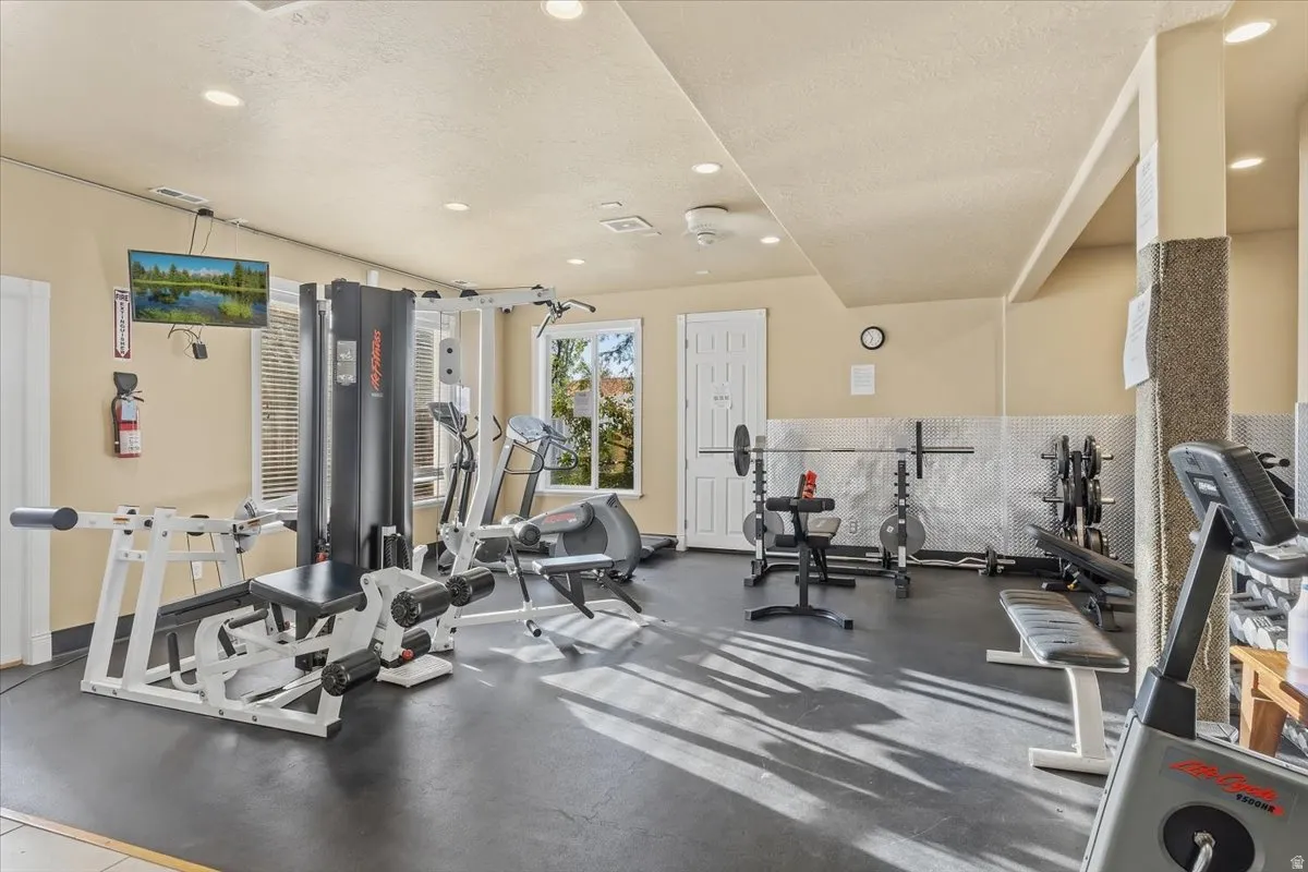 Dedicated fitness area featuring durable rubberized flooring, recessed lighting, and ample natural light from multiple windows