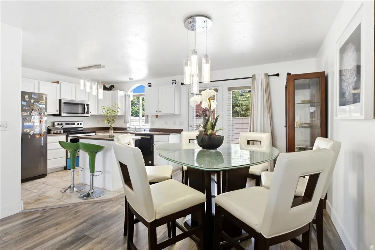 Open-concept kitchen and dining area featuring a breakfast bar with white cabinetry, stainless steel appliances, and a wood-finish flooring