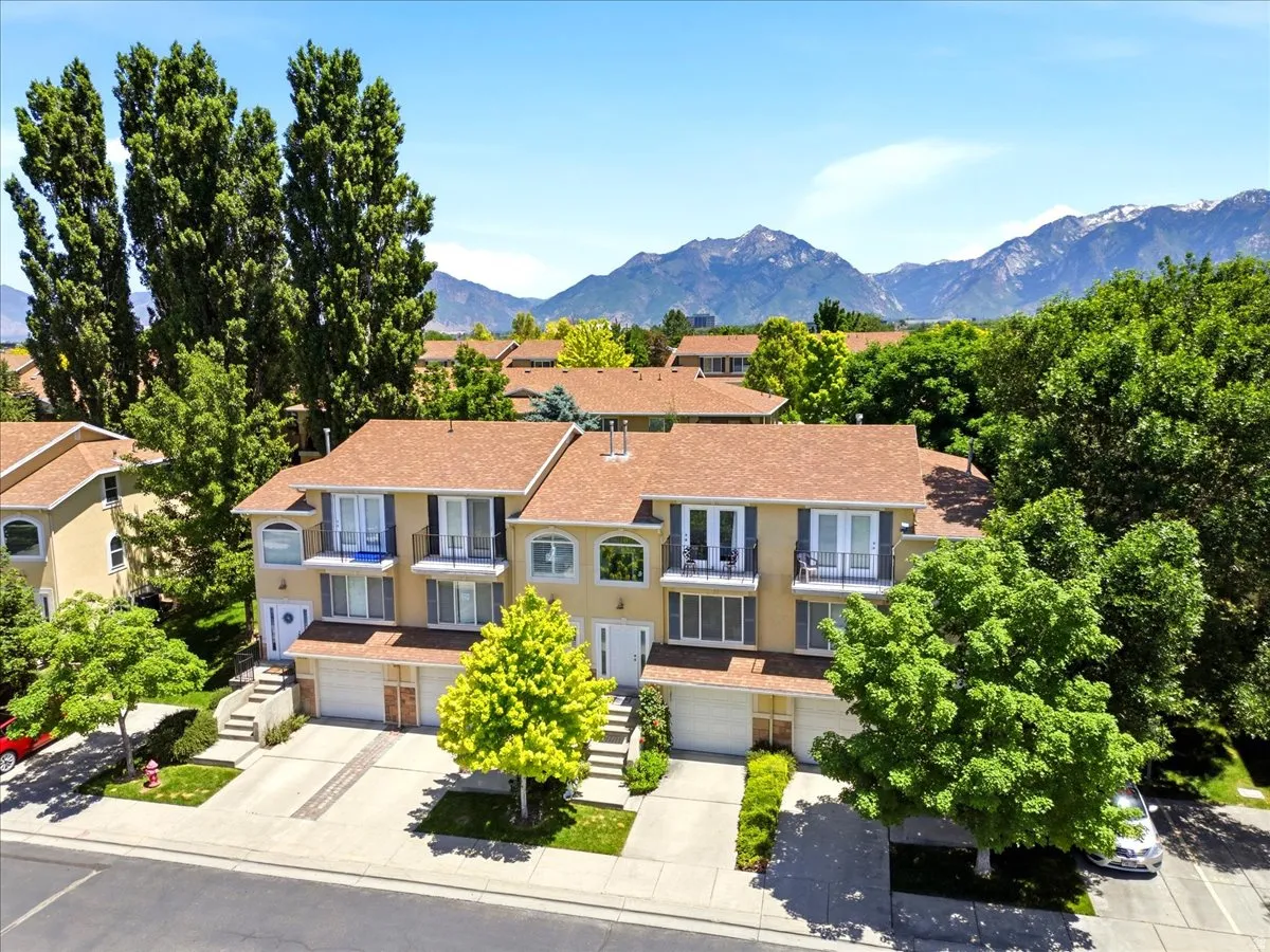 Townhome exterior featuring balconies with wrought iron railings, an arched window, attached garages, and mature landscaping