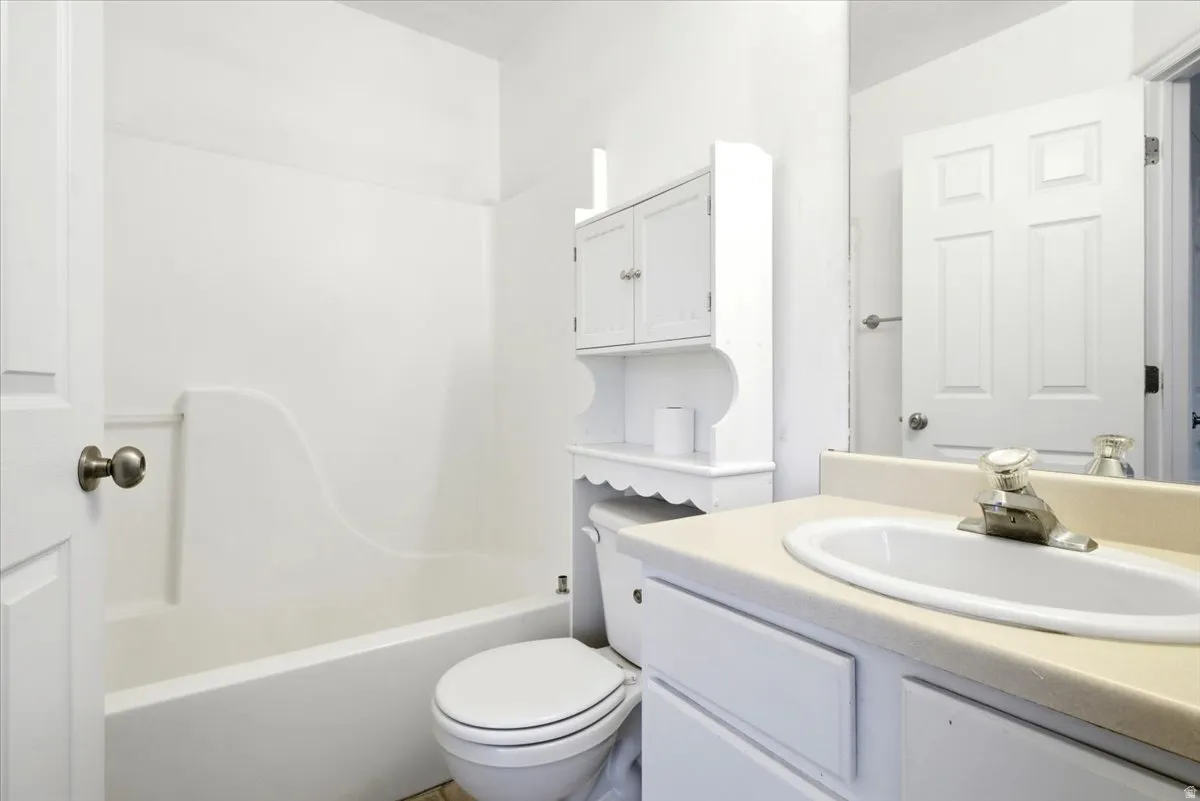 Bathroom featuring a white vanity with an integrated sink, a white toilet, and a white tub/shower combination