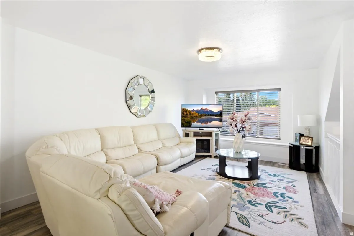 Bright living area featuring white walls, wood-finish flooring, a contemporary ceiling light fixture, and a window with horizontal blinds