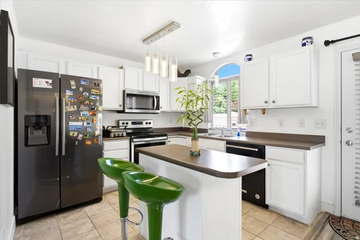 Contemporary kitchen featuring white cabinetry, stainless steel appliances, a center island with countertop seating, a decorative pendant light fixture, and tile flooring