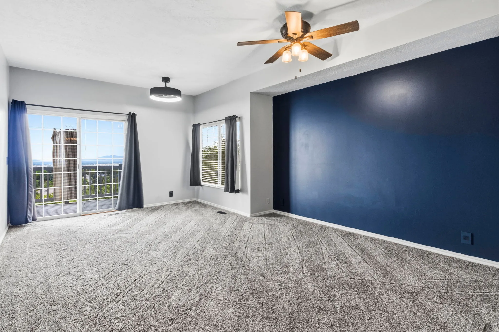 Expansive room with neutral carpet, a bold accent wall, and a ceiling fan with integrated lighting
