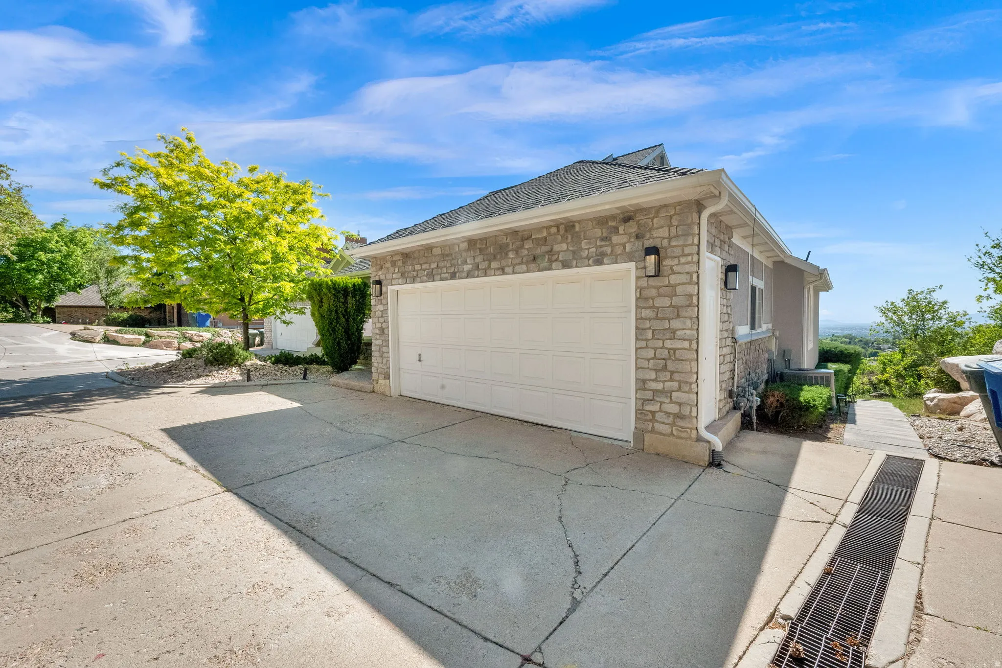 Attached garage with a white panel door, stone veneer facade, dual exterior sconces, and a concrete driveway