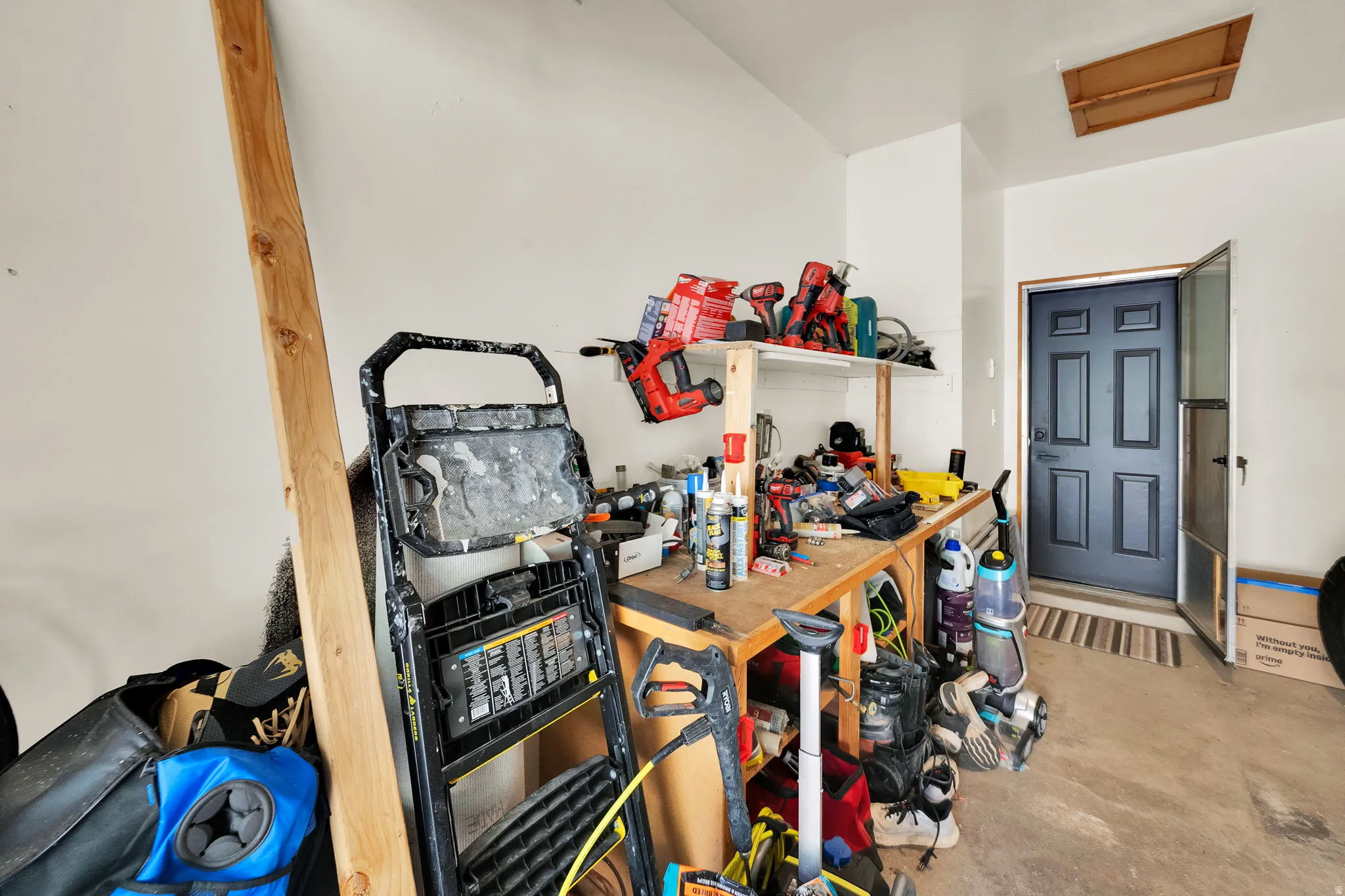 Utility space featuring a workbench with shelving, a concrete floor, an overhead access panel, and a paneled entry door with a screen door