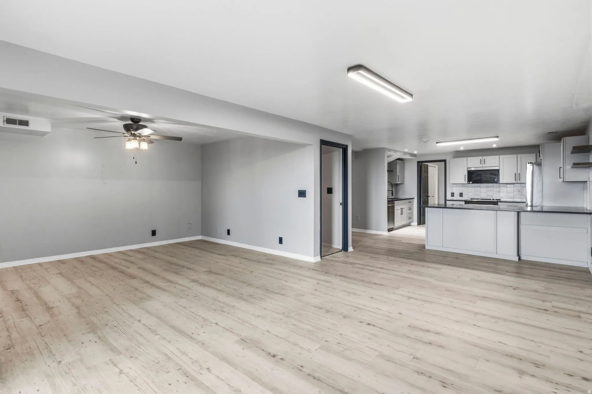 Spacious open-concept living area with wood-finish flooring, a ceiling fan, and recessed lighting