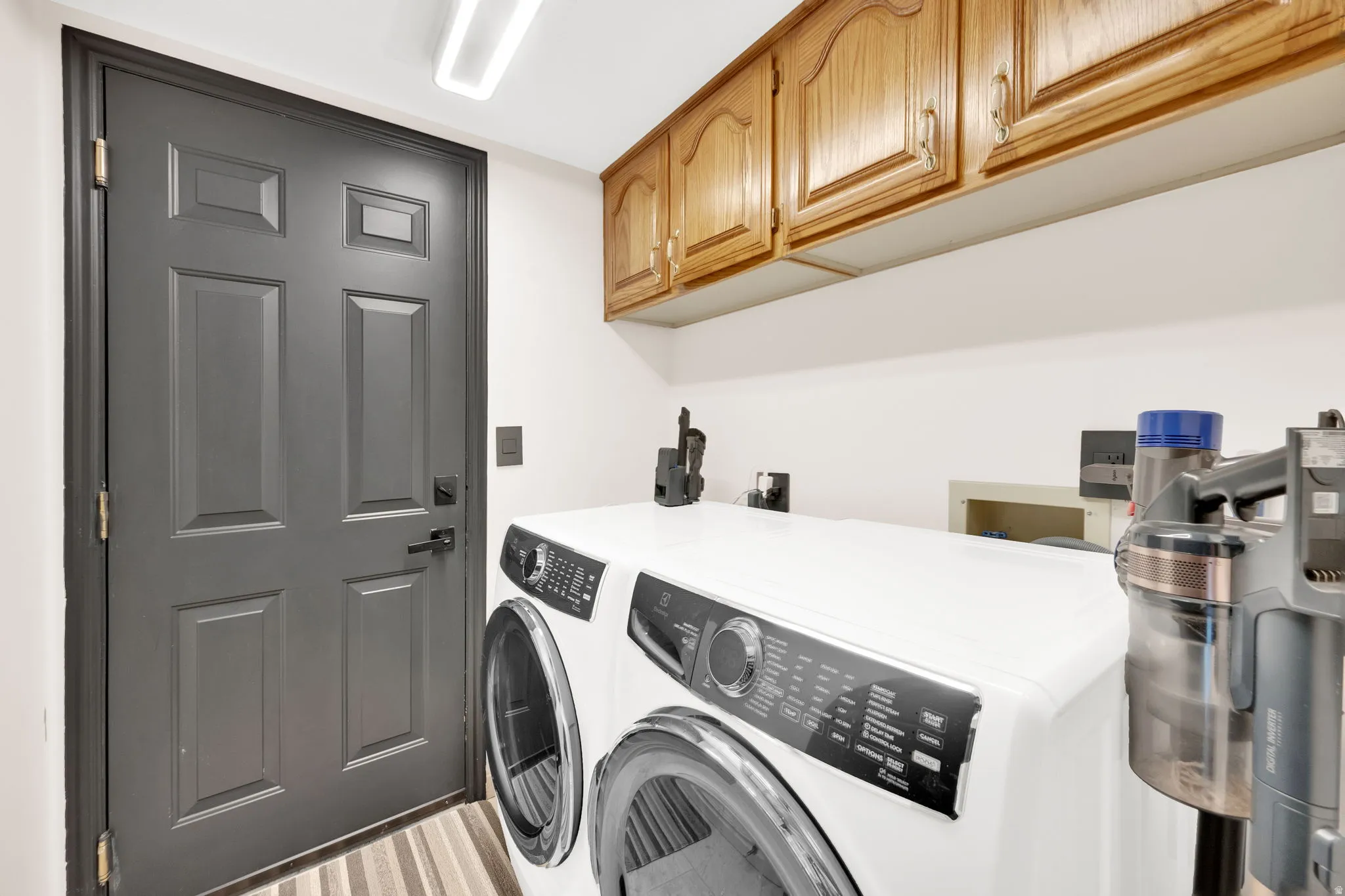 Functional utility space featuring wood-finish upper cabinetry, a paneled door with dark hardware, and a striped floor covering