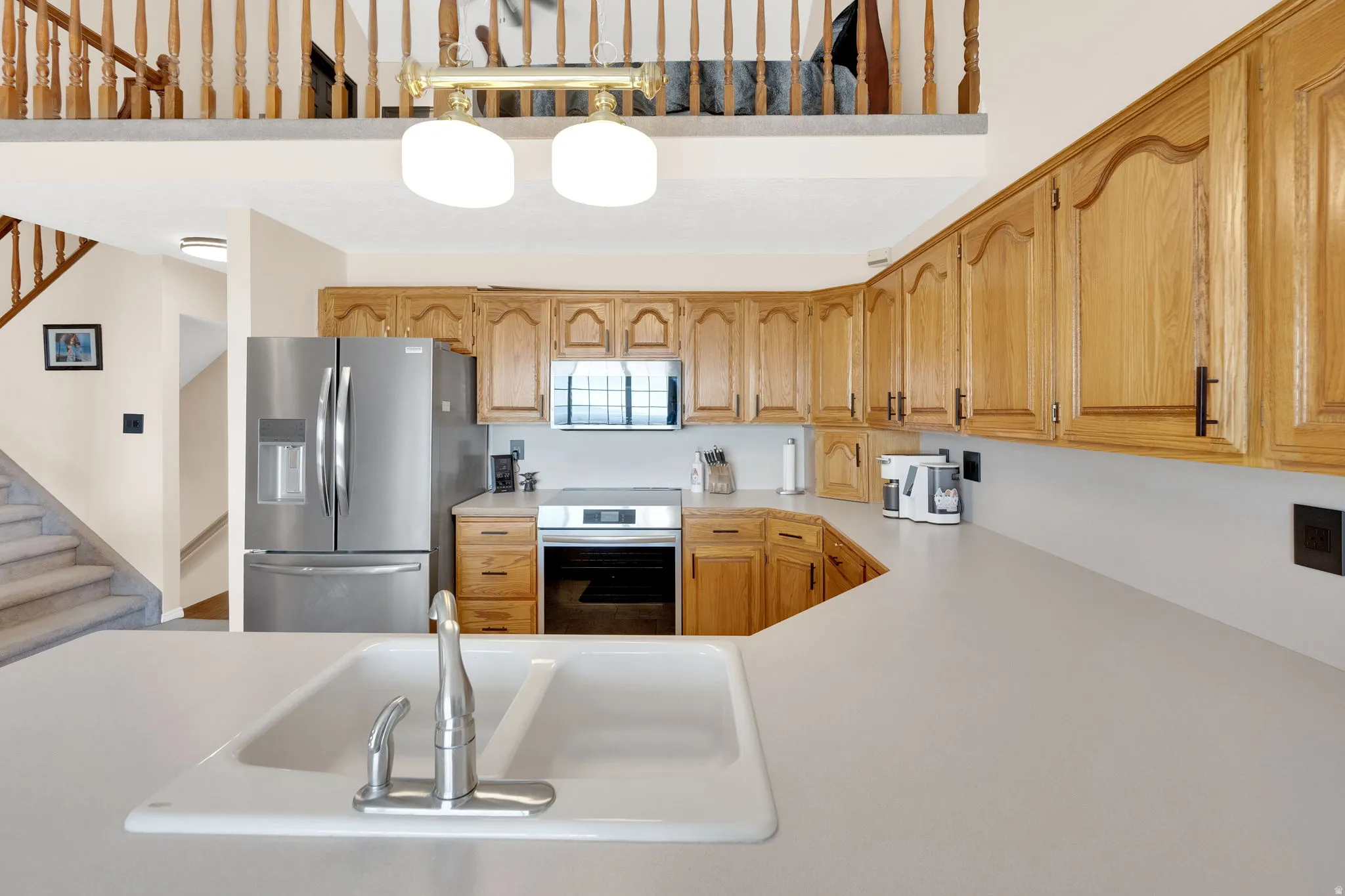 Kitchen featuring abundant wood cabinetry, an integrated white sink with a chrome faucet, stainless steel appliances, and solid surface countertops