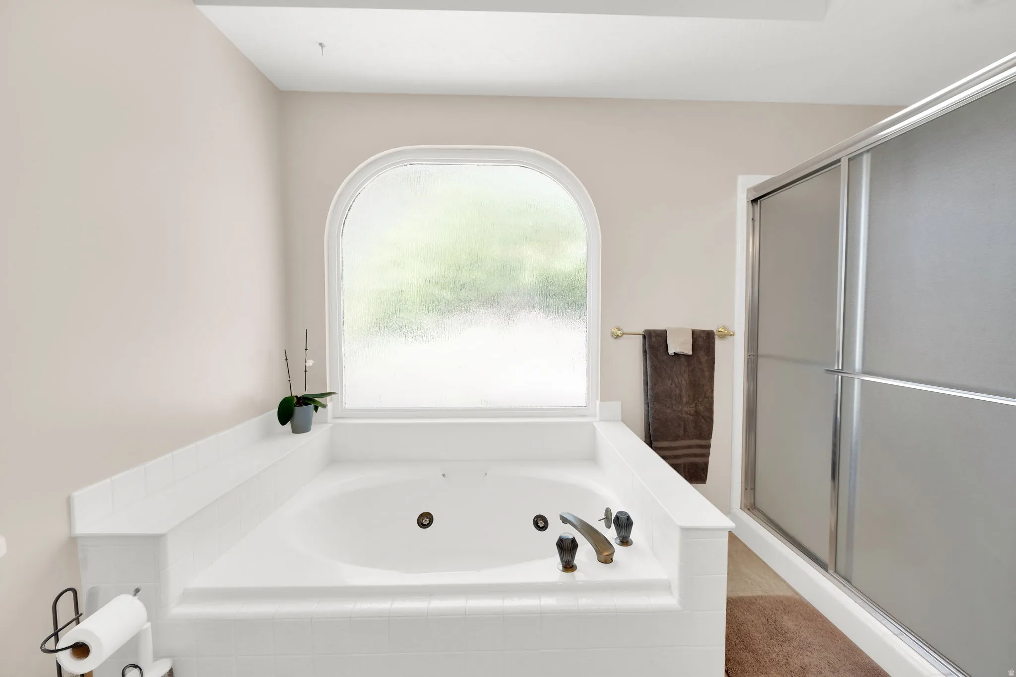 Soaking tub with tiled surround and an arched privacy window, complemented by a separate enclosed shower with frosted glass doors