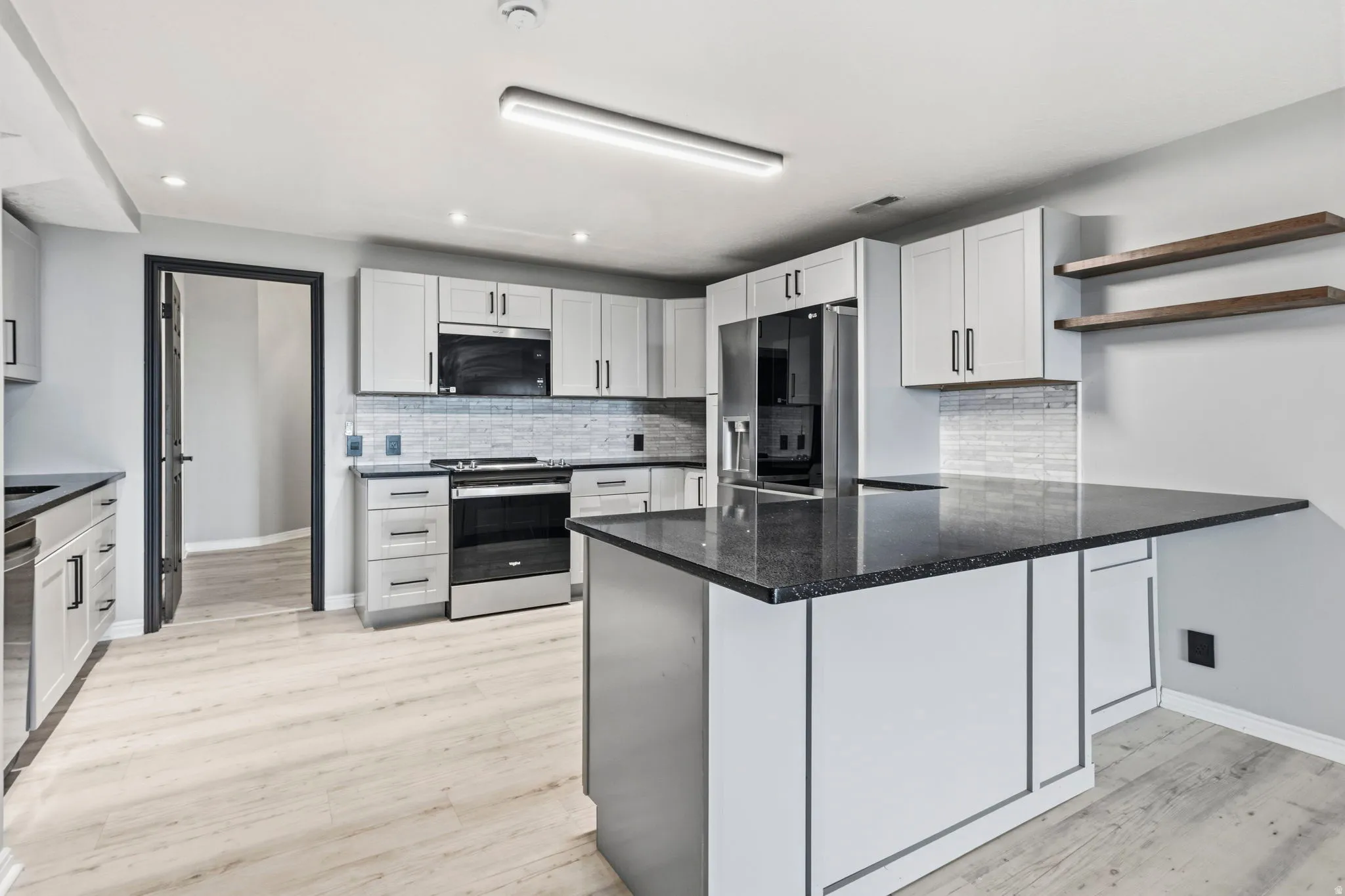 Kitchen featuring wood-finish flooring, light grey cabinetry, black countertops, and stainless steel appliances