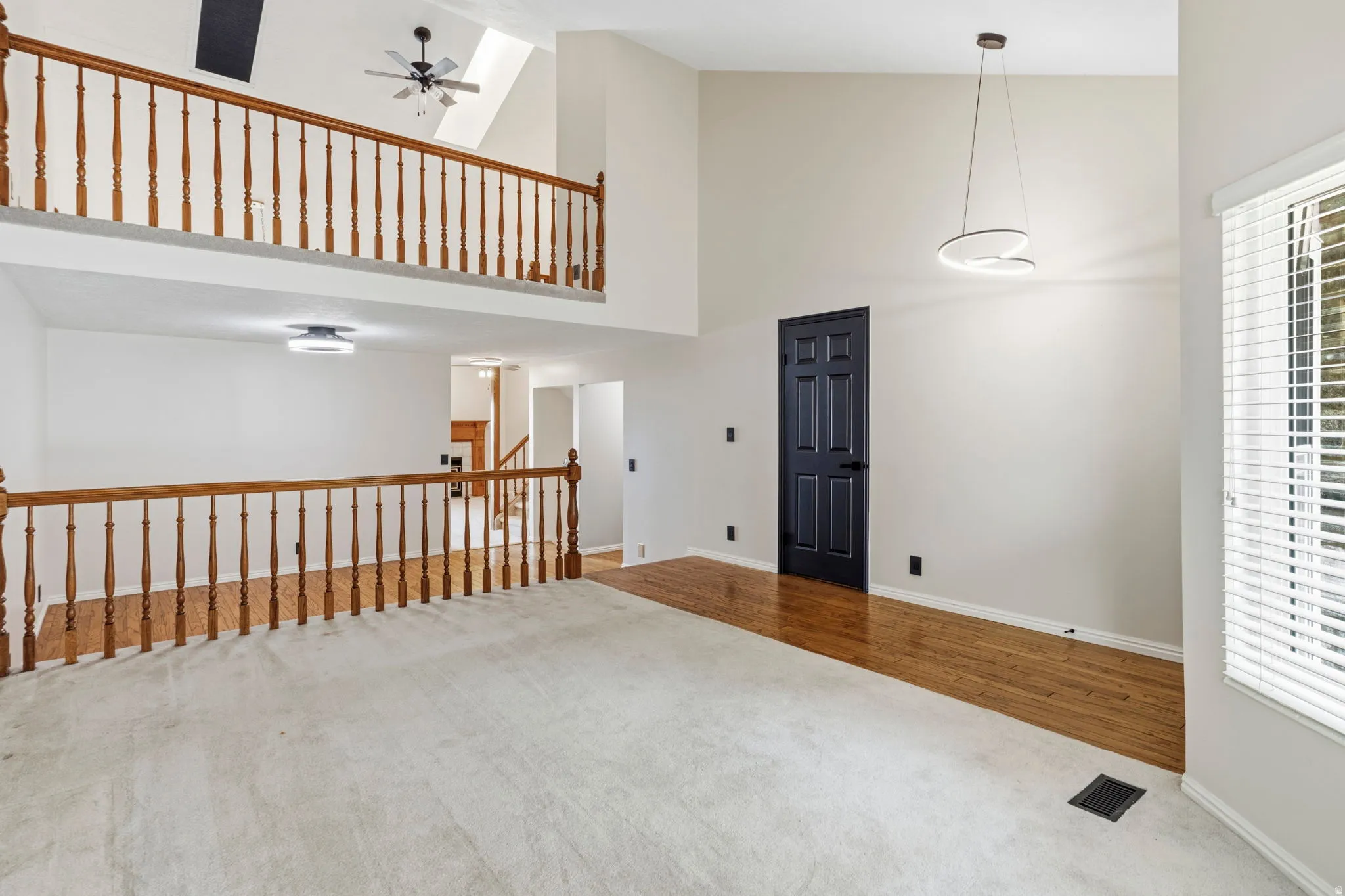 Vaulted ceilings, wood flooring, black interior door, contemporary pendant lighting, and an overhead ceiling fan