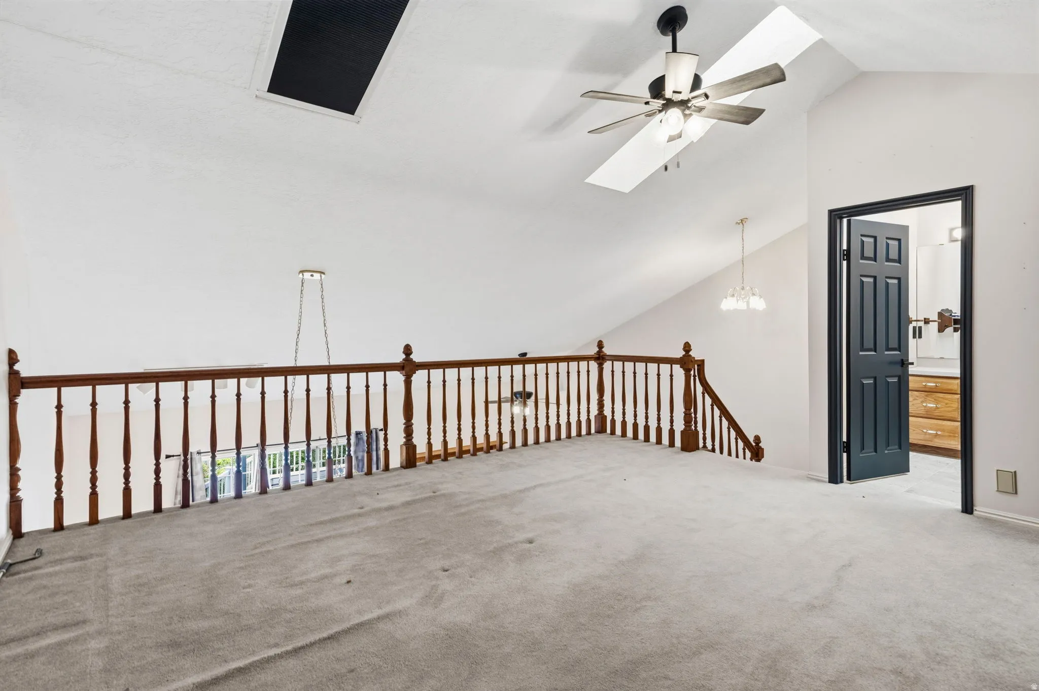 Vaulted ceiling featuring a ceiling fan, a skylight, and a wood railing