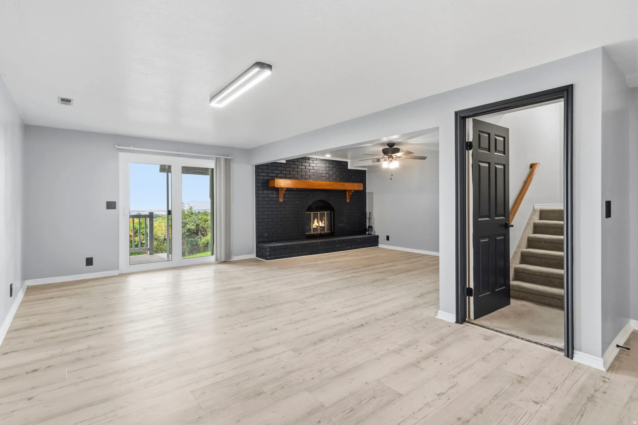 Spacious room with wood-finish flooring, a black brick fireplace with a wood mantel, and sliding glass doors