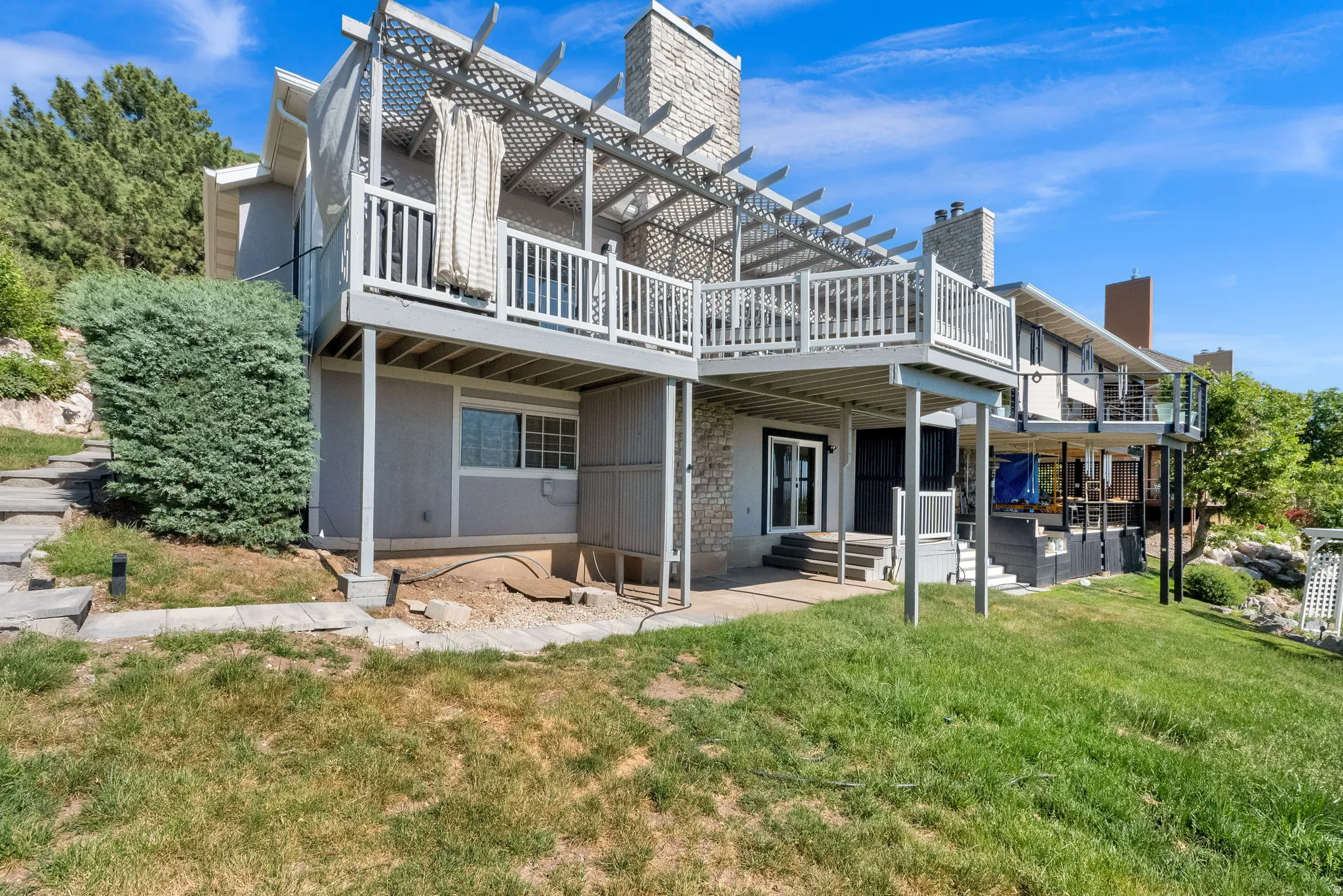 Multi-level outdoor living spaces featuring a pergola-covered deck, a lower patio, and a stone chimney