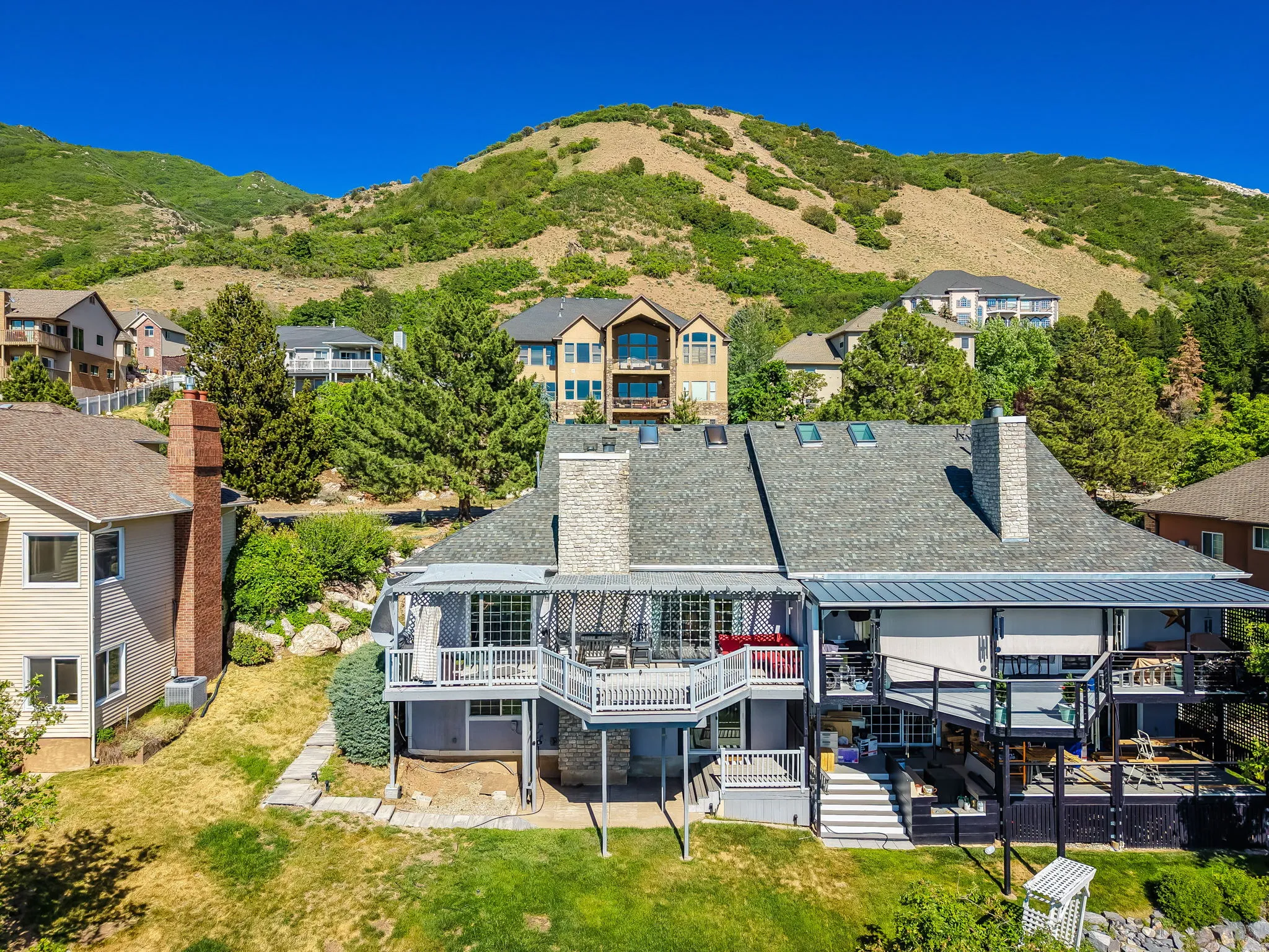 Multi-level property with two stone chimneys and a shingle roof featuring multiple skylights