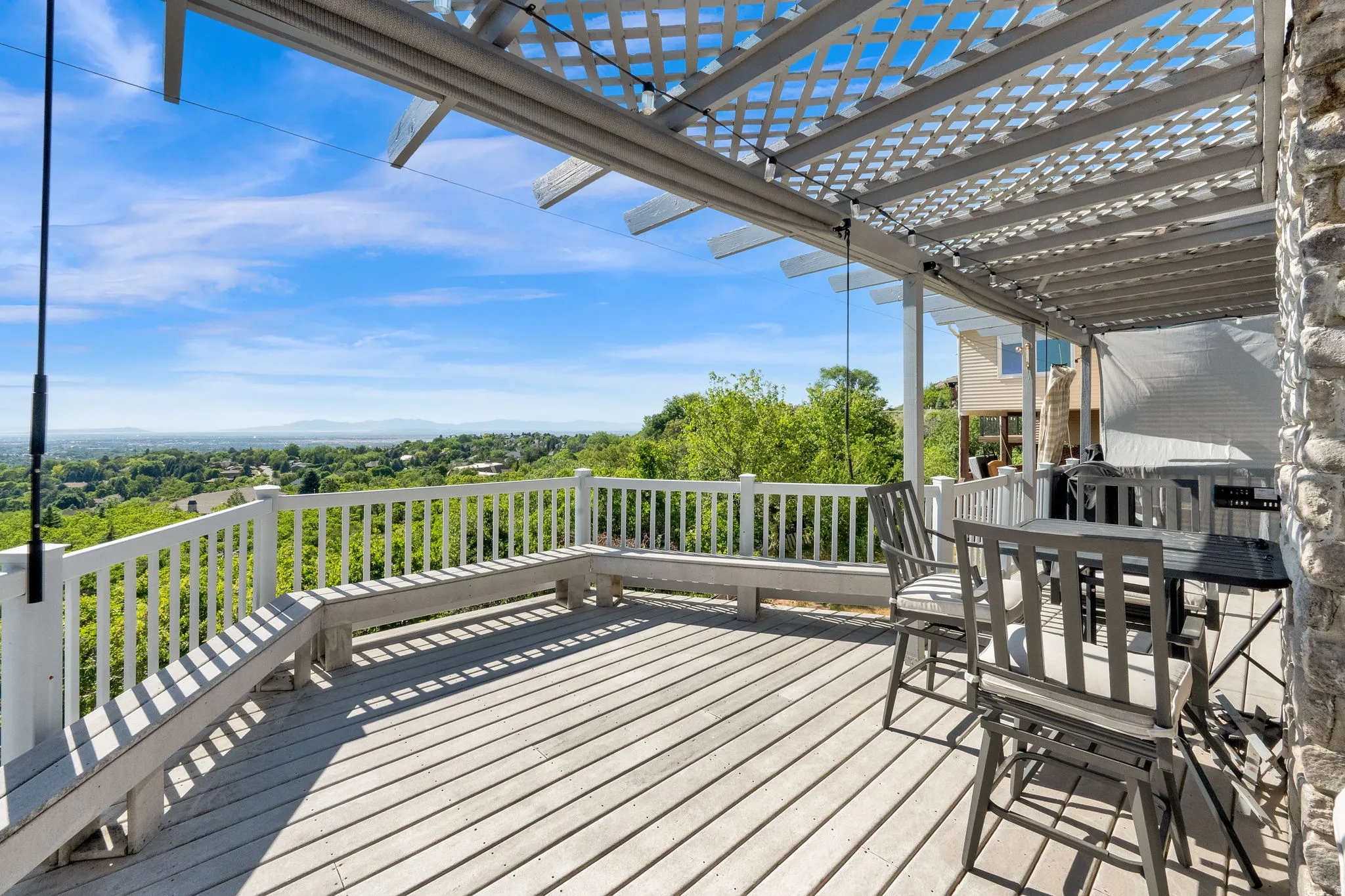 Spacious outdoor deck featuring a slat-style wood pergola, built-in bench seating, durable decking, and a stone-clad exterior wall