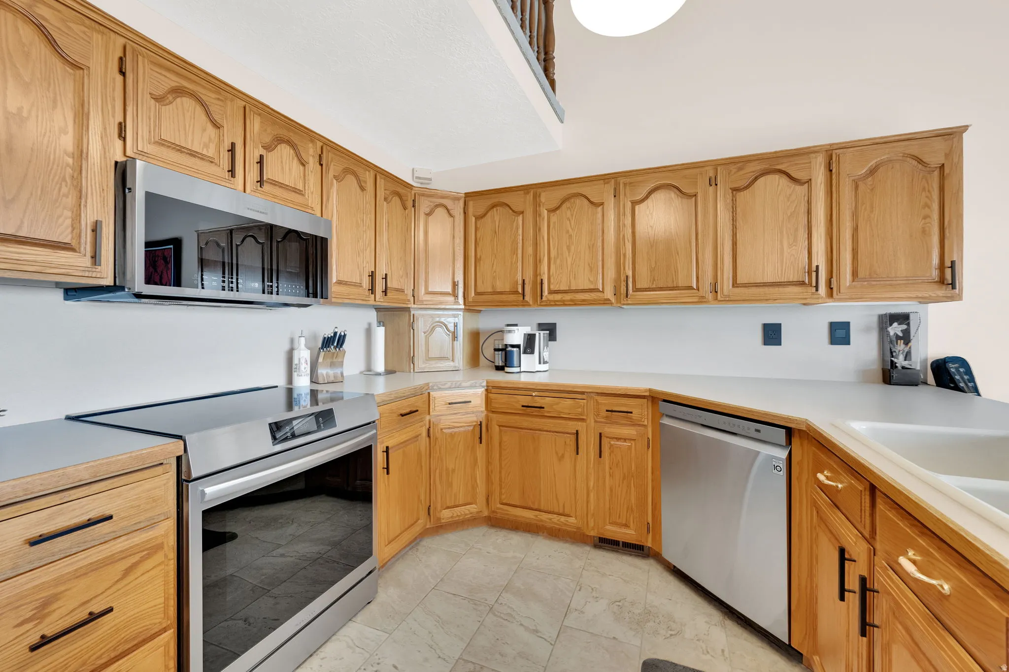 Wood-finish cabinetry with black hardware, white countertops, and stainless steel appliances, including an oven/range and dishwasher