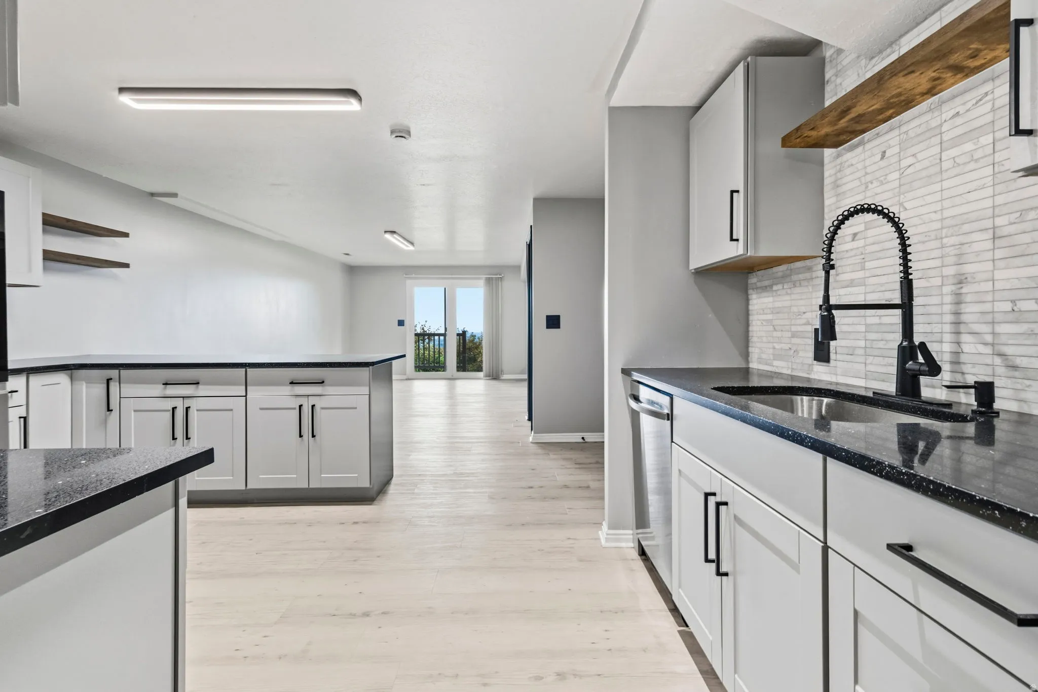 Kitchen featuring light cabinetry, dark countertops, a stainless steel sink with a matte black faucet, and a tiled backsplash