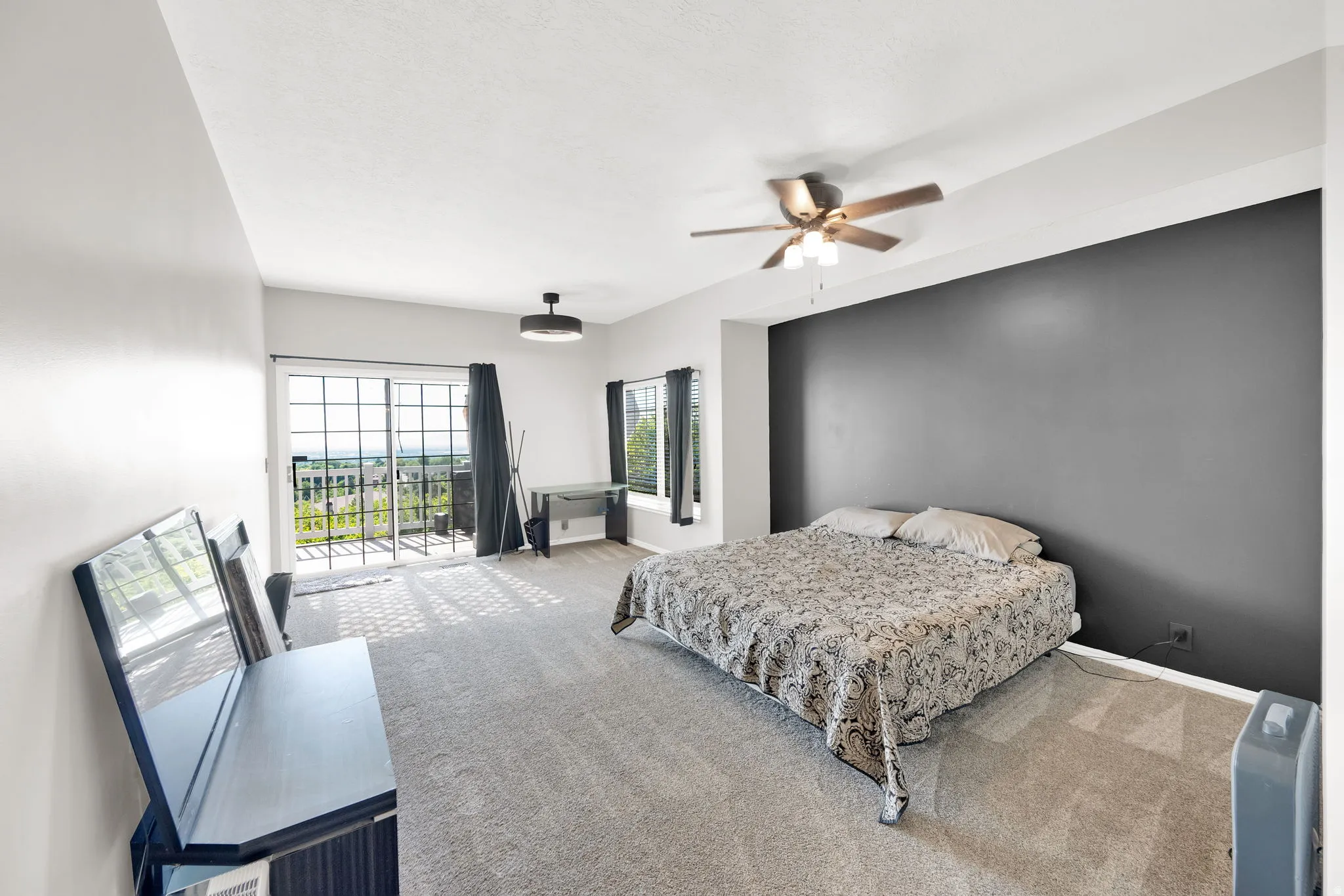 Spacious carpeted room featuring a large sliding glass door, an additional window, and a ceiling fan
