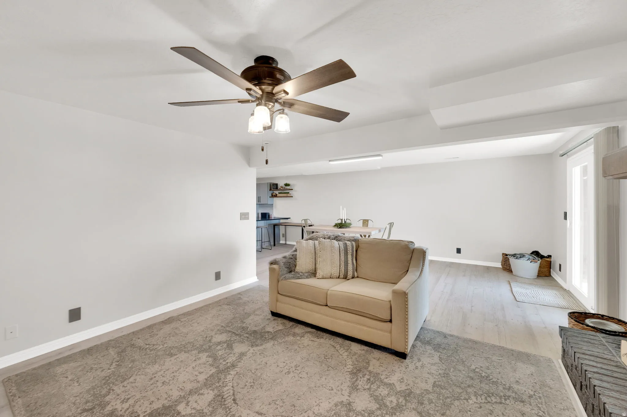 Open-concept living space featuring a ceiling fan, light wood-finish flooring, and crisp white walls