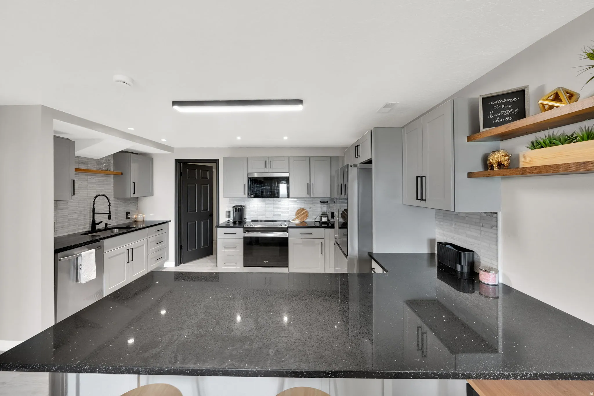 Contemporary kitchen featuring dark countertops, light gray cabinetry with dark hardware, stainless steel appliances, and a tiled backsplash