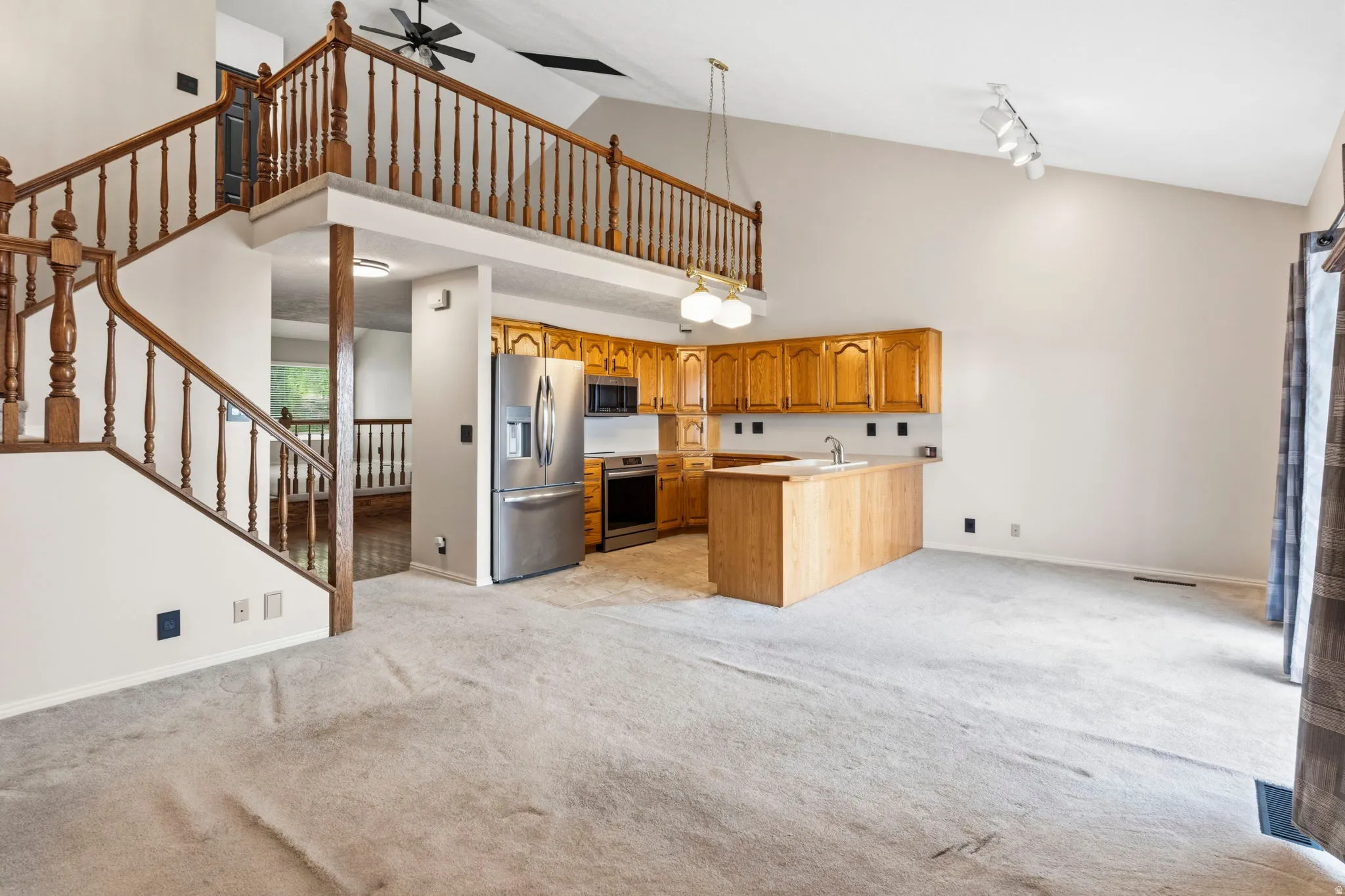 Vaulted ceiling with track lighting, open-concept kitchen with wood cabinetry, stainless steel refrigerator and range, and wood finish island with sink