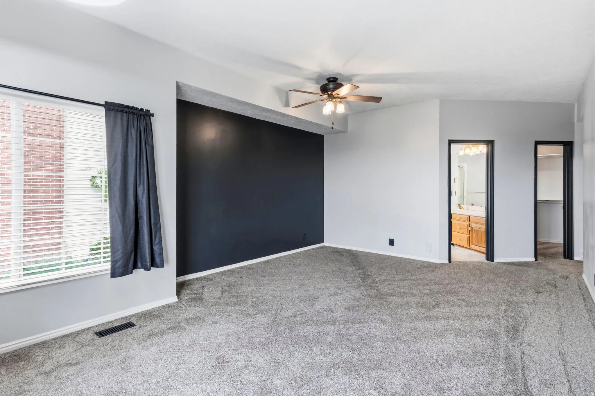 Carpeted room with a dark accent wall, ceiling fan, and window with blinds