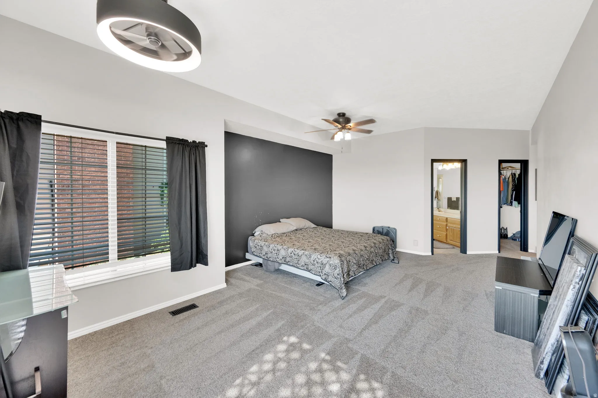 Spacious carpeted room featuring a prominent window, a vaulted ceiling, and two ceiling fans