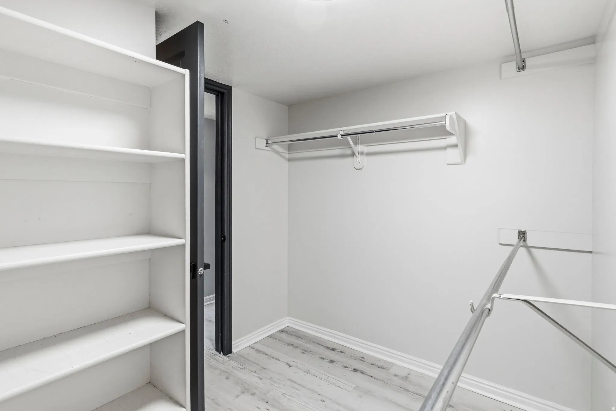 Walk-in closet featuring white built-in shelving, multiple hanging rods, and wood-finish flooring