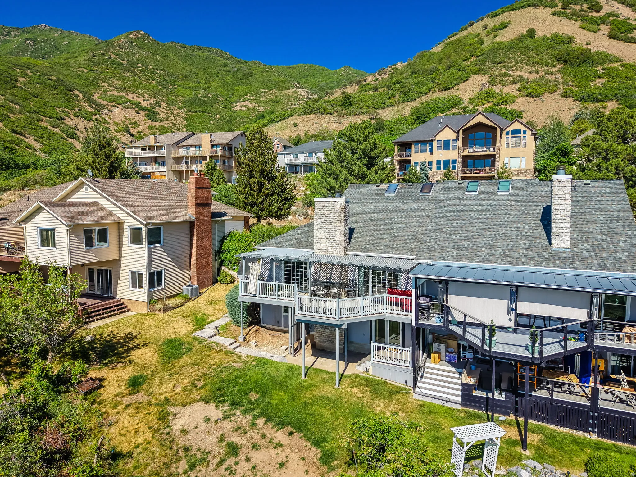 Multi-level residence featuring multiple decks, a gray shingle roof, and two prominent stone chimneys