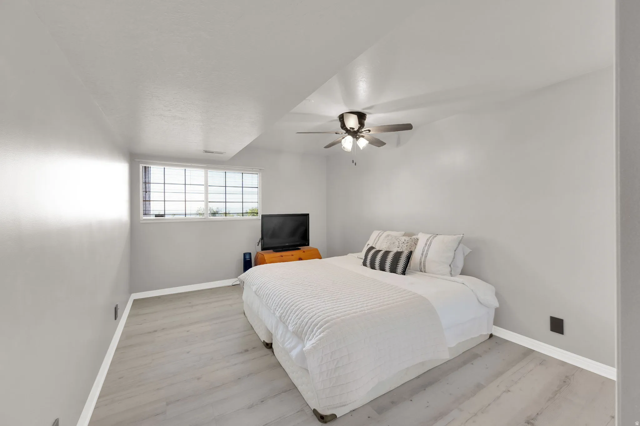 Room featuring light gray walls, wood-finish flooring, a multi-pane window, and a ceiling fan with integrated lighting