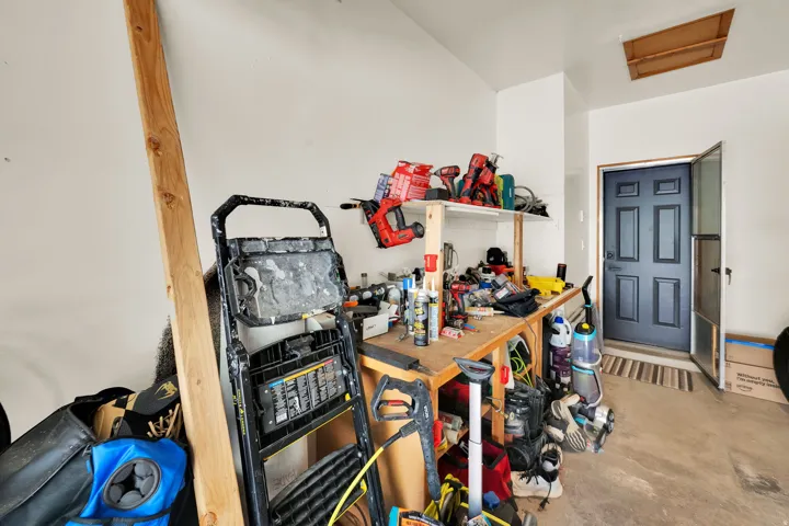 Utility space featuring a workbench with shelving, a concrete floor, an overhead access panel, and a paneled entry door with a screen door