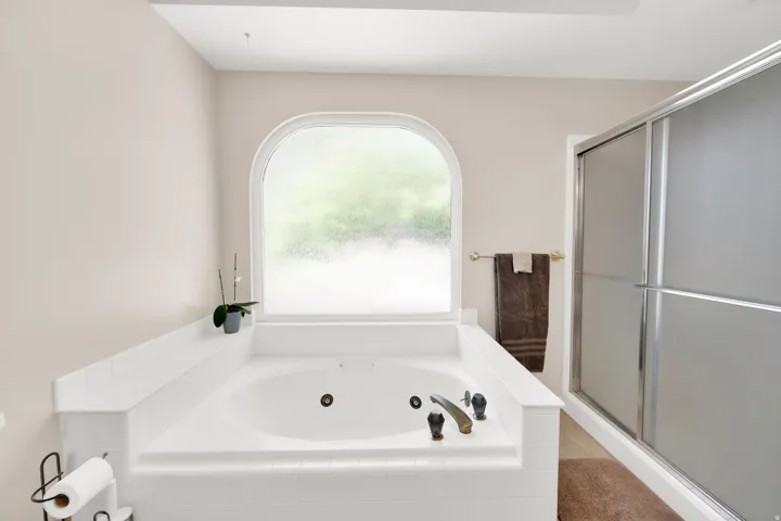 Soaking tub with tiled surround and an arched privacy window, complemented by a separate enclosed shower with frosted glass doors