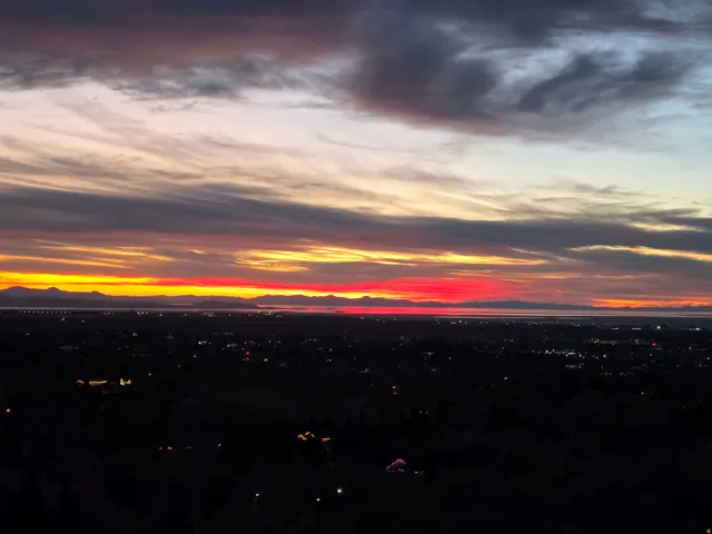 Expansive evening horizon featuring a vibrant sunset sky, distant mountain range, and scattered city lights